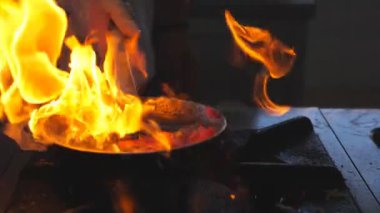 Detail view on flaming skillet in hand of professional chef. Male cook mixing and frying vegetables cooking tasty flambe style dish for visitors of restaurant. Concept of cooking. Slow mo Front view.