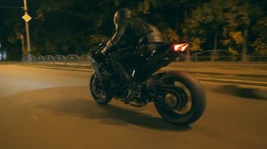 Motosikletli, gece yolunda motosikletiyle yarışıyor. Miğferli genç adam akşam caddesinde modern spor motosikletle hızlı gidiyor. Alacakaranlıkta bisiklet süren adam. Özgürlük ve macera kavramı. Yan görünüm.