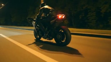 Night City caddesinde, modern motorsikletle hızlı giden bir adam. Motosikletli, boş yolda motosikletiyle yarışıyor. Alacakaranlıkta bisiklet süren adam. Özgürlük ve macera kavramı. Düşük açı. Yakın plan.