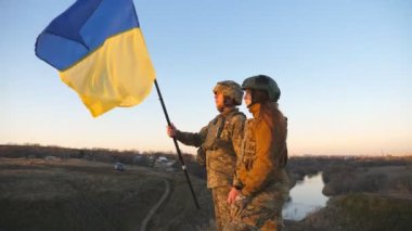 Soldiers of ukrainian army standing at the hill and waving flag of Ukraine. People in military uniform and helmet lifted up yellow-blue flag. Victory against russian aggression. Invasion resistance.