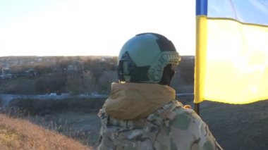 Ukraynalı asker kız günbatımının arka planında ulusal bayrağı kaldırıyor. Askeri üniformalı genç bayan asker tepenin zirvesinde Ukrayna bayrağı sallıyor. Savaşın zaferi. Dolly vurdu..