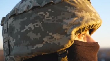 Kasklı ve kar maskeli Ukraynalı asker bakışları. Gün batımında umutla bekleyen genç bir asker. Rus saldırısına karşı zafer. Rusya ve Ukrayna arasındaki savaş. Dolly vurdu..