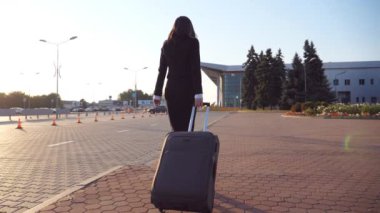 Bavullu tanınmayan iş kadını iş gezisine gitmek için havaalanına yürür. Yüksek topuklu ayakkabılı bir kadın sokakta bavuluyla yürüyor. Arka planda güneş parlıyor. Yavaş çekim. Yakın çekim..