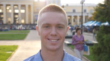 Genç mutlu iş adamının portresi gülümseyen ve duygularıyla kameraya bakan şehir manzarasının arka planına bakan. Şehir ortamında duran yakışıklı adama yaklaş. Dolly vurdu..