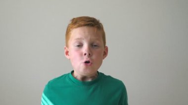 Mutlu kızıl saçlı çilli çocuğun portresi. Sevimli yakışıklı bebek başarıyı alkışlıyor ve baş parmağını kaldırıyor. Yüzünde neşe ifadesi olan erkek çocuğun duygularını kapat. Yavaş çekim.