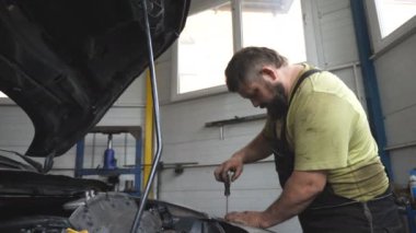 Atölyede ya da serviste tamir edilmeden önce otomobil tamircisi arabayı söküyor. Profesyonel tamirci araç kaputu altında çalışır. Otomobili özel bir aletle tamir eden adam. Bakım ve tanı kavramı