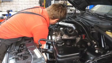 Tamirci oto servisinde araba bakımı yapıyor. Profesyonel tamirci atölyede otomobil motorunu kontrol ediyor. Garajda kaputun altında çalışan bir adam. Otomobil tanısı konsepti. Yavaş çekim.