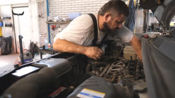 维修工在车间或维修车间修理汽车的发动机 专业汽车机械师在车篷下工作 有胡子的人在车库里检查汽车马达 维护和诊断的概念 — 图库视频影像