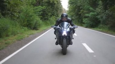Kırsal Orman Yolu 'nda modern spor motosiklet süren kasklı genç bir adam. Motosikletli, tahta yolda motosikletiyle yarışıyor. Yolculuk sırasında bisiklet süren adam. Özgürlük ve macera kavramı. Ön görünüm.