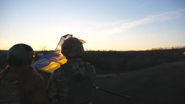 ウクライナ軍の兵士は日没を背景にウクライナの国旗を掲揚した 軍の制服を着た人々が黄色の旗を持ち上げた ロシアの侵略に対する勝利 侵入抵抗概念 — ストック動画