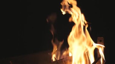 Siyah arka planda, mangal ağacında yanan odun parçalarından kırmızı alevler yükselir. Yakacak odun geceleri barbeküde yanar. Karanlıkta metal mavisi içinde şenlik ateşi. Sıcaklık ve dinlenme kavramı. Yavaşça kapat.