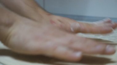 Restorandaki mutfak masasında pizza için un hamuru şekillendiren şefin ellerini kapat. Aşçının erkek kolları mutfakta ahşap bir yüzey üzerinde hamur işi oluşturuyor. Yemek hazırlama kavramı. Yavaş çekim.