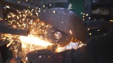 Metal öğüten profesyonel işçilerin elleri. Endüstriyel imalatta çelik testeresi. Birçok parlak kıvılcım sıcak metalden uçar. Garajdaki kesim makinesini gördüm. Yavaş çekim. Yakın çekim..