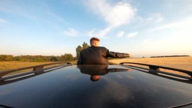 Arabanın sunroof 'unda duran ve kır yolunda giderken rüzgarla oynayan genç adam. Tanınmayan bir adam yolculuk ve esintinin tadını çıkarıyor. Seyahat ya da özgürlük konsepti. Arka plan.