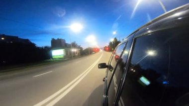 Gece şehir otobanında giden siyah cipin görüntüsü. Akşamları otomobille şehir sokaklarında dolaşmak. Araç otoban boyunca hızla ilerliyor. Şehir trafiği. Yolculuk konsepti. Bakış açısı.