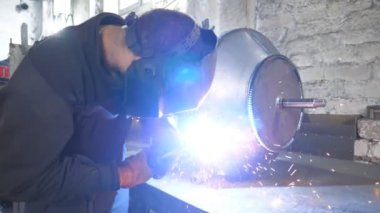 Endüstriyel üretimde koruyucu maske kaynak işçisi. Kaynakçı, metal fabrikasında iki çelik detayı arasında bağlantı kuruyor. Metal kaynak yapan adam. Yavaşça kapat..