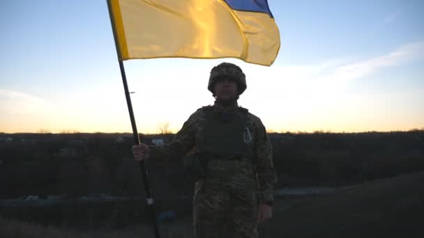 ウクライナの旗を振っているウクライナ軍の兵士 軍の制服を着た男とヘルメットは日没時に旗を持ち上げた ロシアの侵略に対する勝利 侵入抵抗の概念 スローモーション — ストック動画