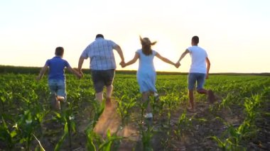 İki oğlu el ele tutuşan ve gün batımında yeşil alanda koşan genç ebeveynler. Anne ve baba ve çocuklar çayırlarda koşup el kaldırıyorlar. Aile kavramı. Arka plan Yavaş çekim.