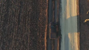 Tarlanın yakınındaki kırsal yoldan geçen kamyonetin hava görüntüsü. Sonbaharda tarla sürülen çayırın yakınına giden siyah bir arabanın üzerinde uçmak. Çiftlik arazisinin yakınına giden off road aracı..