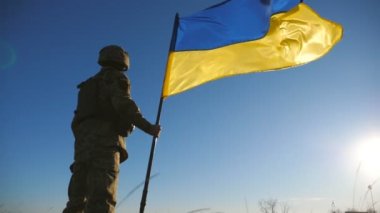 Ukrayna ordusunun erkek askeri mavi gökyüzüne karşı ulusal bayrağı kaldırıyor. Askeri üniformalı adam Ukrayna bayrağı sallıyor. Rus saldırısına karşı zafer. İstila direnişi. Düşük görünüm.