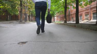 Kentin sokaklarında resmi giyinen kendine güvenen iş adamının bacaklarına geri bakış. Toplantıya yürürken çantasında telefon olan tanınmamış bir girişimci. Ofis işi konsepti. Yavaş çekim.