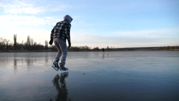 フィギュアスケートの若い男の影に氷の上で滑りに続く 凍った川でスケートする男 スカイ湖の氷の表面に反映されます 寒い冬のアクティブなレジャー 健康的なライフスタイルの概念 スローモーション — ストック動画