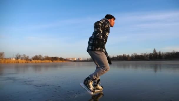 美しい夕日の間に氷の上で滑りフィギュアスケートの男の靴 凍った川でスケートをしている若者 輝く太陽の氷の湖の表面に反映されます 冬の寒い日にアクティブなレジャー スローモーション — ストック動画