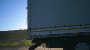 Kargo karavanı olan, otobanda giden ve malları taşıyan kamyonun yan görüntüsü. Kamyon kırsal yoldan geçerek hedefe gidiyor. Kamyon römorkunu kapatın. Kargo taşıma konsepti. Yavaş çekim.