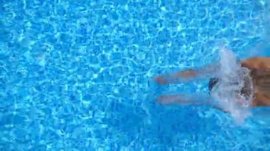 Havuza atlayan ve kristal berrak su sıçratan genç bir kadın manzarası. Güneşli bir günde otelin havzasında su altında yüzen tanınmamış bir kız. Bayan yaz tatilinde dinleniyor. Yavaş çekim.