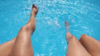 Otelin havuzunda kristal berrak su sıçratan dişi bacaklar. Havzanın kenarında oturan iki arkadaş güneşli bir günde tatilin tadını çıkarıyorlar. Yaz tatili ya da tatil kavramı. Yavaş çekim bakış açısı.