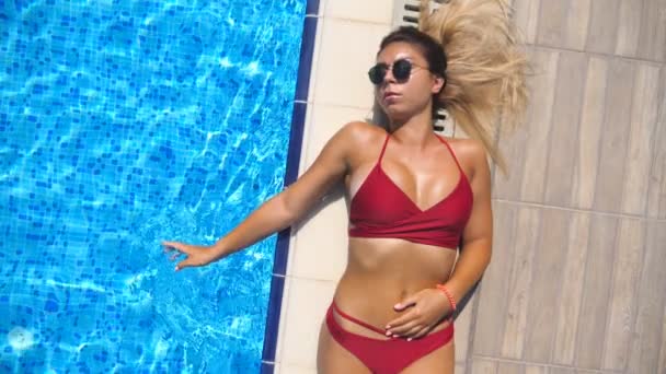 가장자리와 표면에 선글라스에 매력적인 그을린 여자의 클로즈업 수영장 근처에서 일광욕을 — 비디오