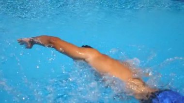 Berrak mavi suyla havuz boyunca yüzen tanınmayan sportif adam. Genç adam yüzme ve yaz güneşli bir günde tatil de rekreasyon keyfini. Tatil veya tatil kavramı. Yan görünüm Yavaş hareket.