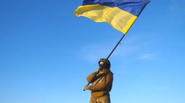 Ukrayna bayrağı sallayan Ukraynalı kadın Ukraynalı asker. Askeri üniformalı ve kasklı bir kadın mavi gökyüzüne bayrak kaldırdı. Rus saldırısına karşı zafer. İstila direnişi kavramı.