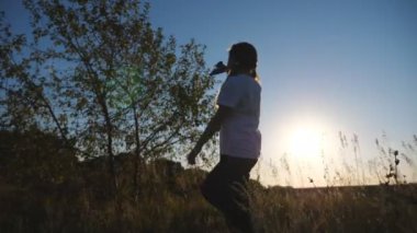 Küçük çocuk kırsalda yürürken uçakla oynuyor. Küçük mutlu kız arka planda güneş ışığına karşı oyuncak uçakla gidiyor. Tasasız çocuk doğayla eğleniyor. Çocukluk hayali konsepti. Yavaş çekim.