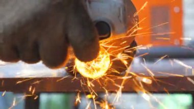 Metal işlemede dairesel testere ile detaylı görüş. Makinistin elleri enstrüman tutuyor ve metali öğütüyor. Garajda ya da atölyede demir kesen bir işçi. Parlak kıvılcımlar uçuşuyor. Kapat..