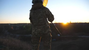 Askeri üniformalı genç bir kadının gün batımının arka planında mavi-sarı bayrak sallarken çekilen resmi. Ukraynalı kadın asker ulusal bayrağı kaldırıyor. Ukrayna topraklarının işgali kavramı