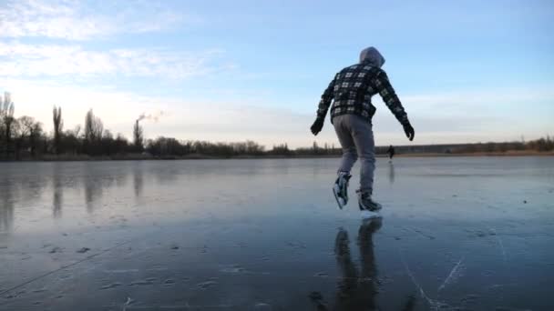 フィギュアスケートの若い男の影に氷の上で滑りに続く 凍った川でスケートする男 スカイ湖の氷の表面に反映されます 寒い冬のアクティブなレジャー 健康的なライフスタイルの概念 スローモーション — ストック動画