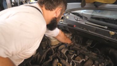 Tamirci oto servisinde araba bakımı yapıyor. Garajda kaputun altında çalışan profesyonel bir tamirci. Sakallı adam atölyede otomobil motorunu kontrol ediyor. Otomobil tanılama kavramı.