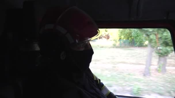 消防車の場所に大きなトラックに乗って制服を着た若い男性消防士 非常用に消防車を運転する設備の整った消防士 命と英雄的職業を救うという概念 — ストック動画