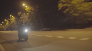 Erkek motorcu, şehir merkezinde modern motosikletiyle hareket ediyor. Gece yolunda parlak farları olan güçlü bir motorsikletle motosiklet süren bir motosikletli. Yolculuk sırasında bisiklet süren genç bir adam. Kapat..