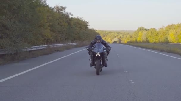 高速道路でスポーツバイクに乗って高速保護ヘルメットに男性バイカーのフロントビュー オートバイ運転手は初秋の田舎道を自転車で移動している 旅行中にバイクを運転する若い男 — ストック動画