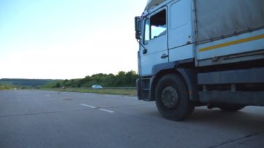 Kamera bir otoyolda sürüş kamyon için izleyin. Arka plan, güzel manzara ile kırsal yoluyla kamyon sürmek. Asfalt, kamyon sürüş tekerlek. Yan görünümü ağır çekim yakın çekim.