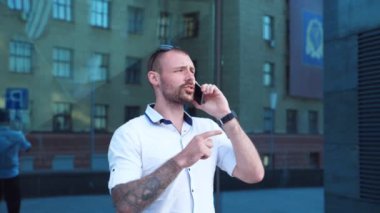 Ofisin yanında telefonla konuşan yakışıklı bir işadamı. Genç iş adamı modern binanın yakınında cep telefonuyla konuşuyor. Dışarıda konuşan kendinden emin bir adamın portresi. Yavaş çekim. Yakın çekim..