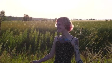Kırsal kesimde fotoğraflara poz veren dövmeli kaygısız serseri kız. Pembe saçlı mutlu bayan hipster gün batımında kırsal kesimde fotoğraflanır. Hippi kadın doğada dinleniyor. Kapat..