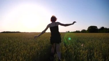 Gün batımında yeşil arpa tarlasında koşan dövmeli mutlu punk kadın. Kaygısız hippi kız buğday tarlasında koşarken eğleniyor. Arka planda güzel manzaralı yaz manzarası.