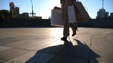 Genç bayan müşteriler alış veriş sonrası alışveriş torbalarını meydanda tutarlar. Modaya uygun bir kadın, şehir caddesinde kağıt paketler taşıyor. Satış ve indirim zamanlarında boş vakit kavramı. Yavaş çekim