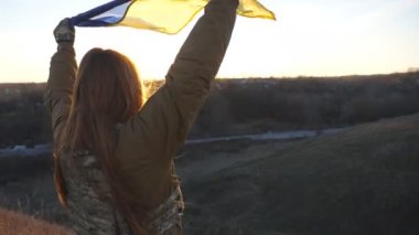 Ukrayna bayrağı sallayan Ukraynalı kadın Ukraynalı asker. Askeri üniformalı kız mavi gökyüzüne karşı sarı-mavi bayrak kaldırdı. Rus saldırısına ve savaşın sona ermesine karşı zafer. Kapat..