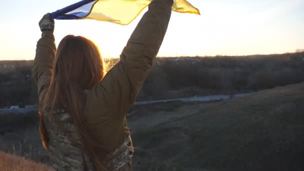 ウクライナの旗を振っている女性ウクライナ軍兵士 軍の制服を着た少女は 青空に対して黄色の青の旗を持ち上げた ロシアの侵略と戦争の終わりに対する勝利 閉じろ — ストック動画