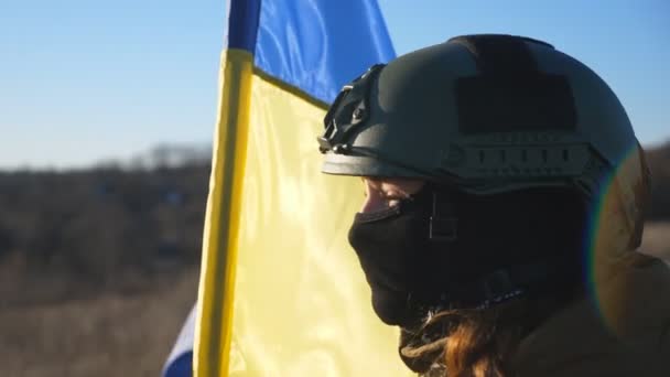 軍事用ヘルメットとバラクラバで少女のドリーショットは 手を振っ国旗を保持しています ウクライナ軍の女性兵士は田舎で青黄色の旗を持ち上げた ウクライナ侵攻 閉じろ — ストック動画