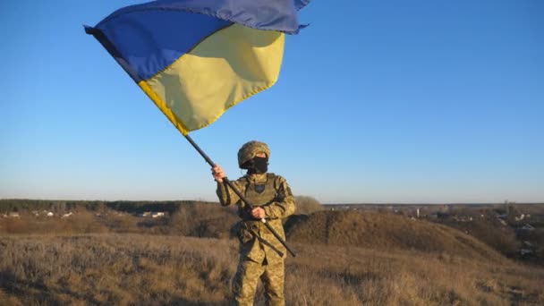 青い空に対してウクライナの軍事制服を着た若い男のドリーショット ウクライナ軍の男性兵士は戦場で国旗を掲揚した ロシアの侵略に対する勝利 戦争の終結 — ストック動画